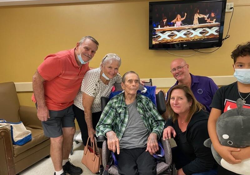 A group of five people posing indoors, one in a wheelchair.